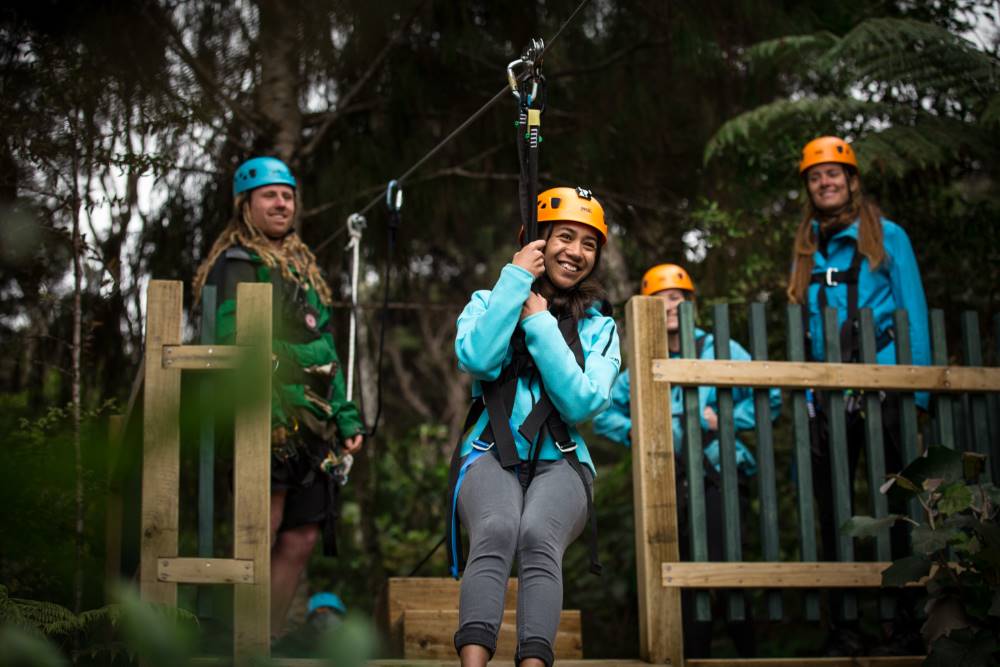 Smiling visitor takes off on a New Zealand zipline adventure through native forest at Driving Creek in Coromandel.